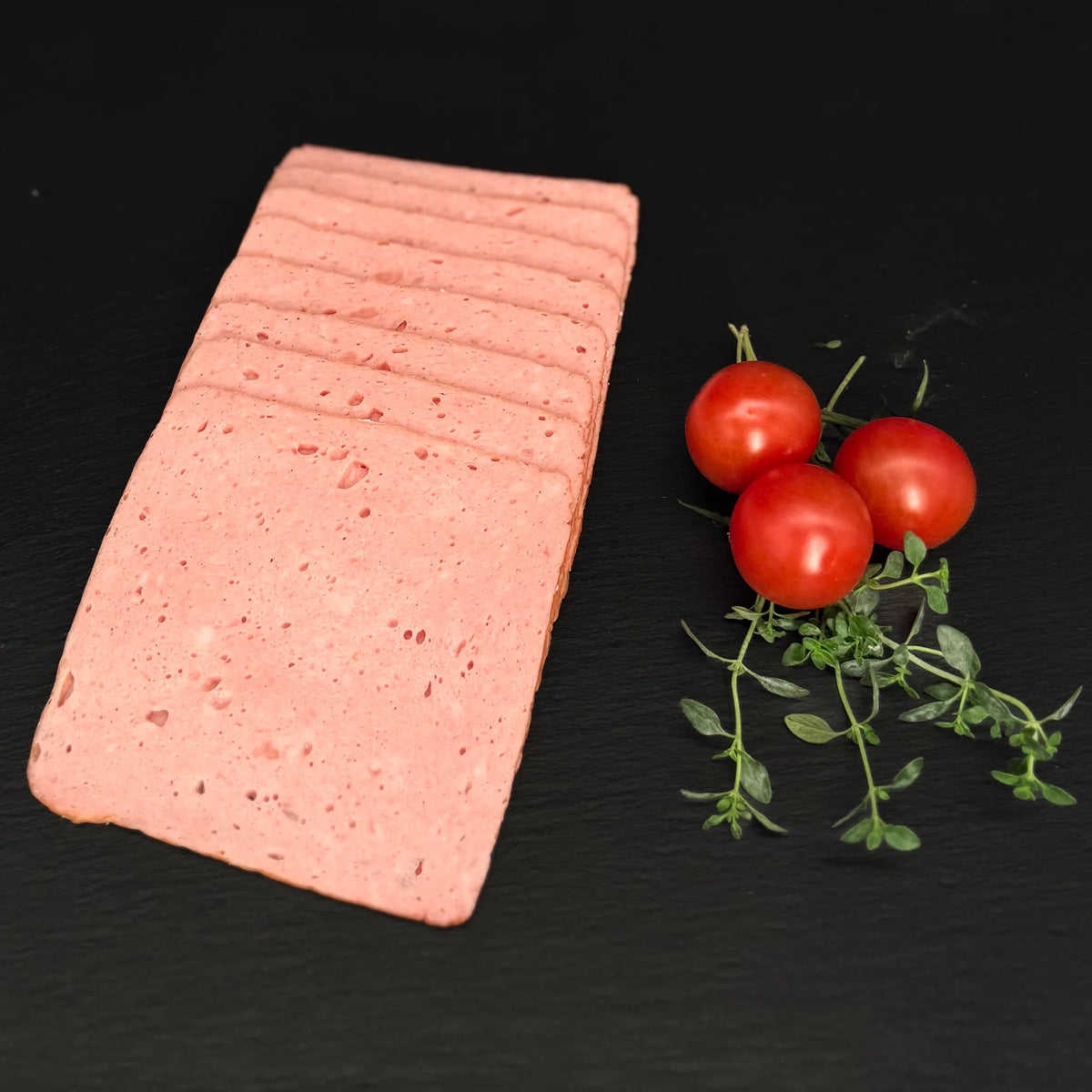Geschnittener Römerbraten, gefächert, auf einer schwarzen Schieferplatte mit Dekoration aus Tomaten und Kräutern.