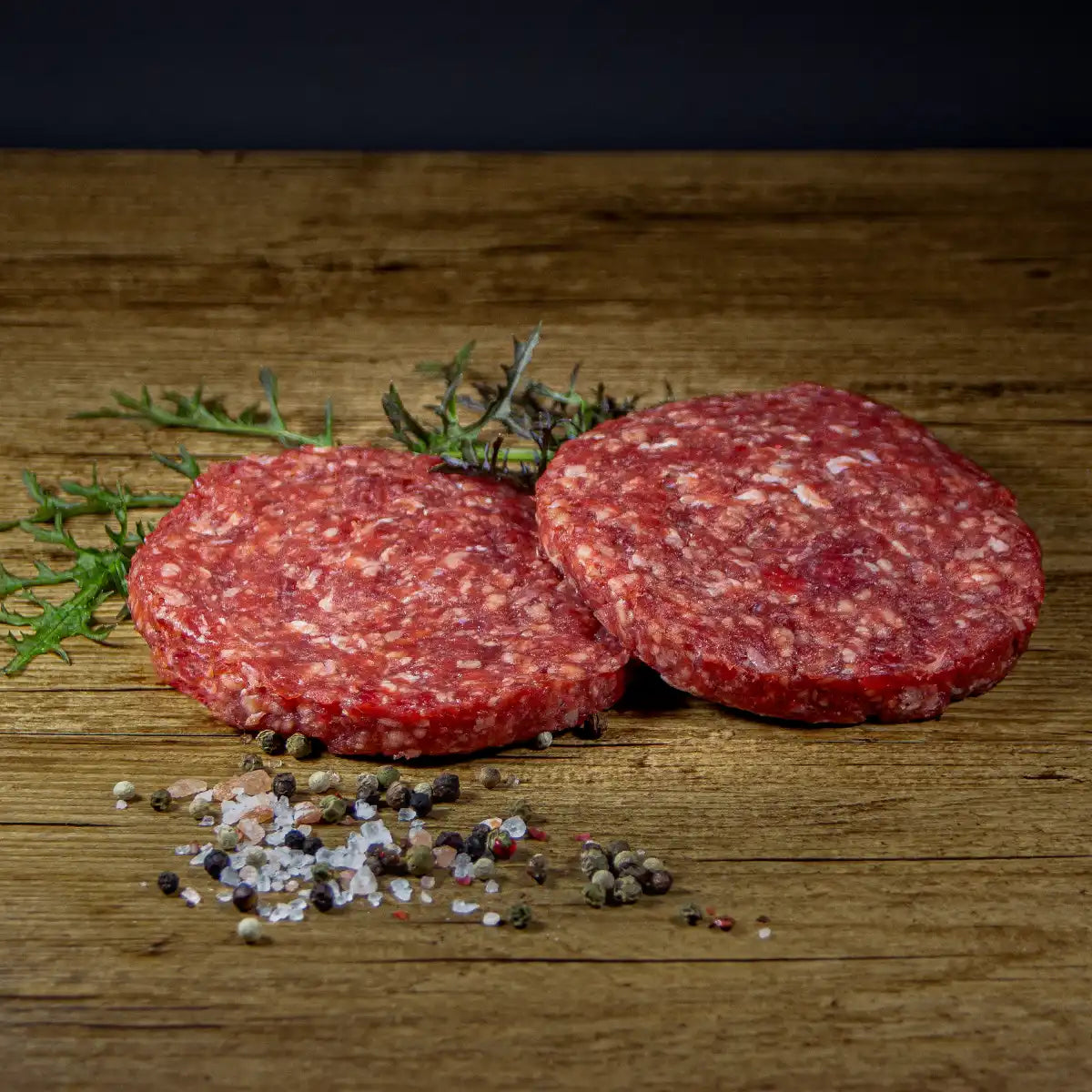Zwei Burgerpatties auf Holzuntergrund davor etwas Salz