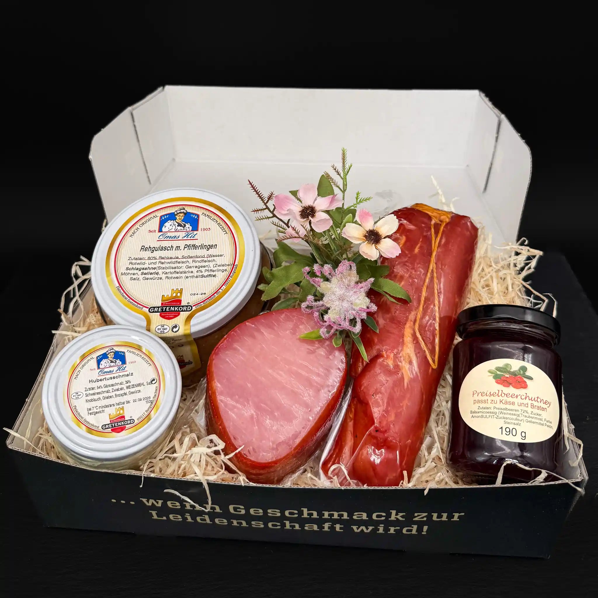 Eine rechteckige Box gefüllt mit einem Glas Hubertusschmalz, Preiselbeerchutney sowie Rehgulasch mit Pfifferlingen sowie einem Lachsschinken und einem geräucherten Schweinefilet.