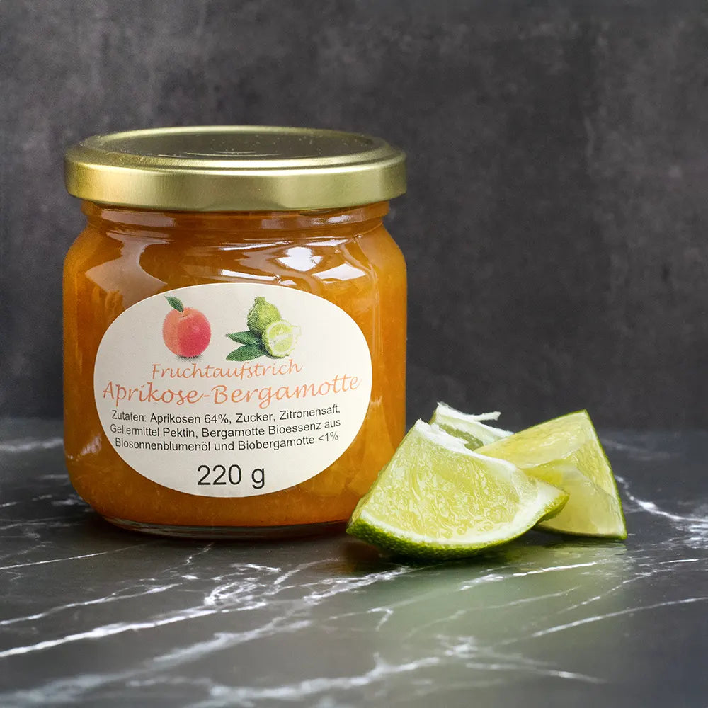 Oranger Fruchtaufstrich im Glas neben geschnittener Bergamotte vor dunkelgrauem Hintergrund.