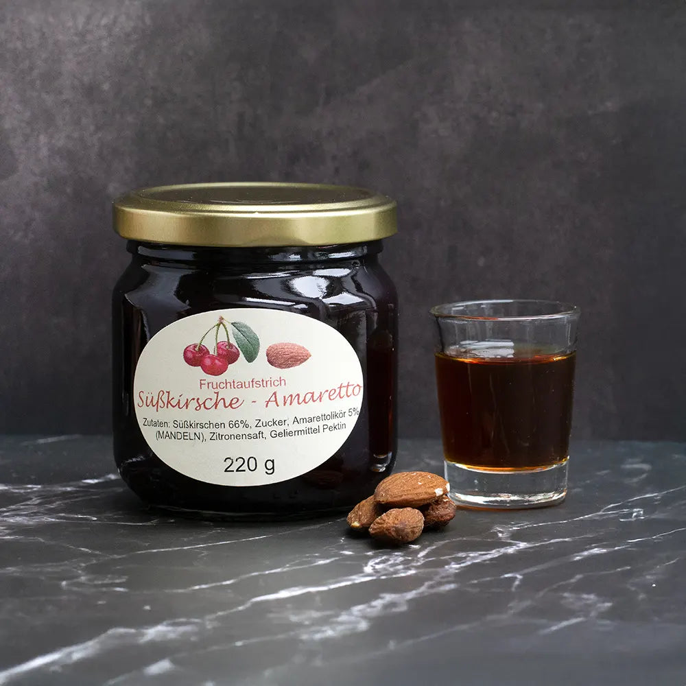 Roter Fruchtaufstrich im Glas neben 4 Mandeln und Schnapsglas mit Amaretto vor dunkelgrauem Hintergrund.