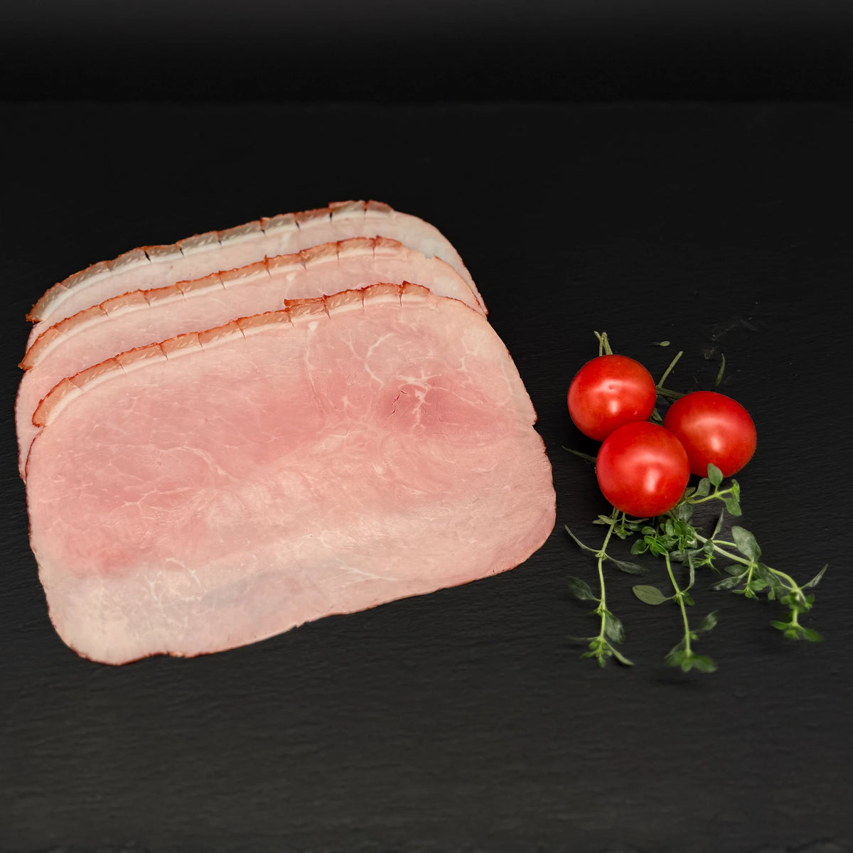 Geschnittener, ofengebackener Krustenschinken, gefächert, auf einer schwarzen Schieferplatte mit Dekoration aus Tomaten und Kräutern.
