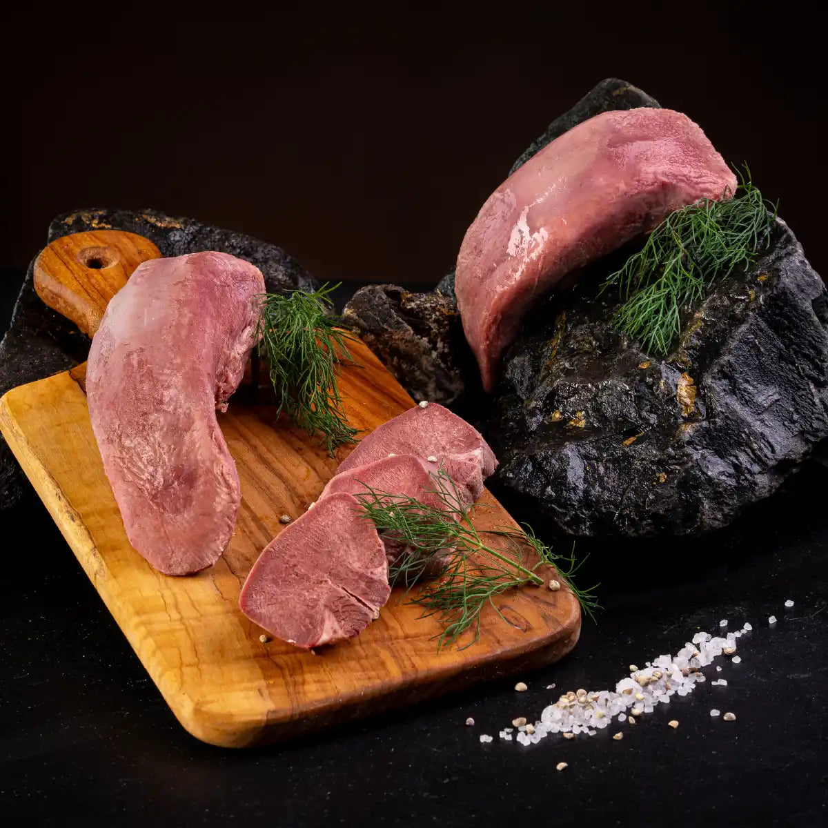 Auf einem hellen Holzbrett liegt ein ganzes Stück Zunge und davor aufgeschnitten einige dicke Scheiben