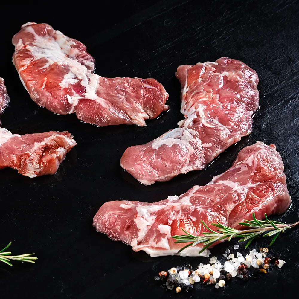 Drei Stücke Kachelfleisch vom Duroc Strohschwein von der Seite vor dunklem Hintergrund.