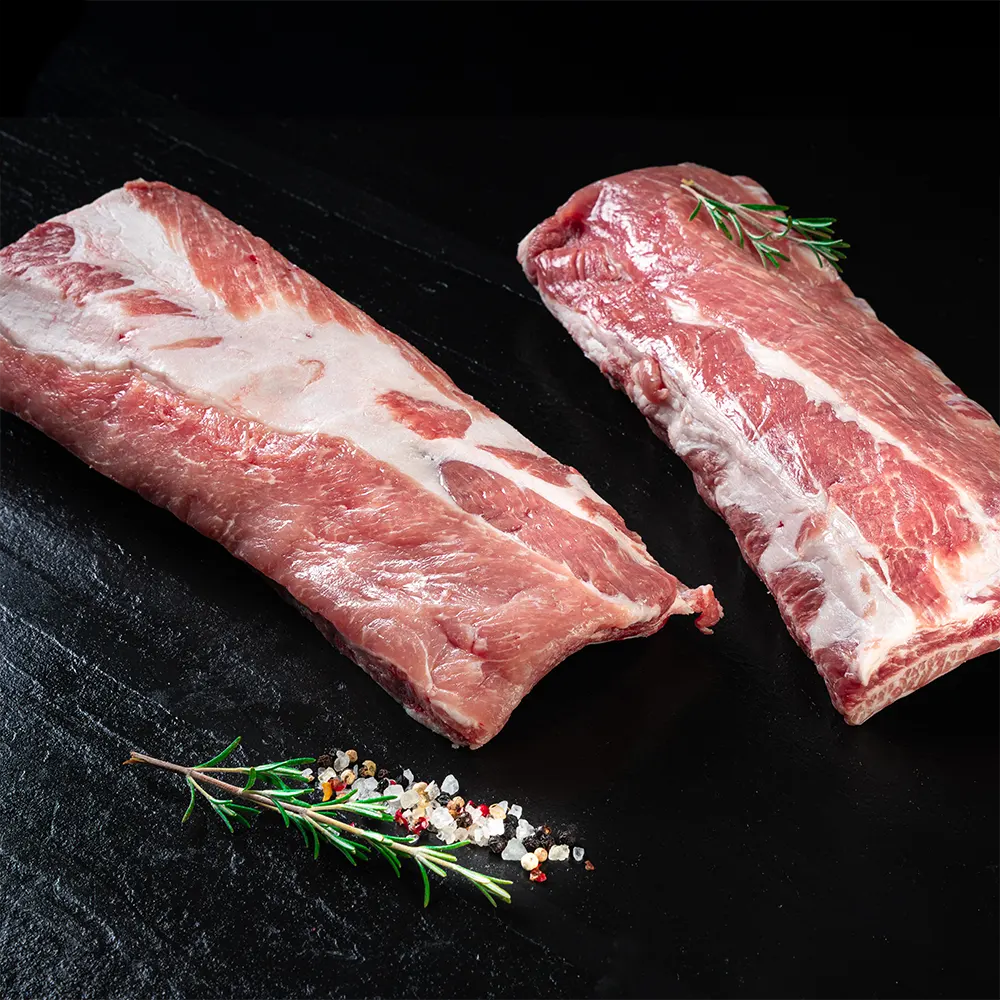 Zwei Spareribs vom Duroc Strohschwein von der Seite vor dunklem Hintergrund.