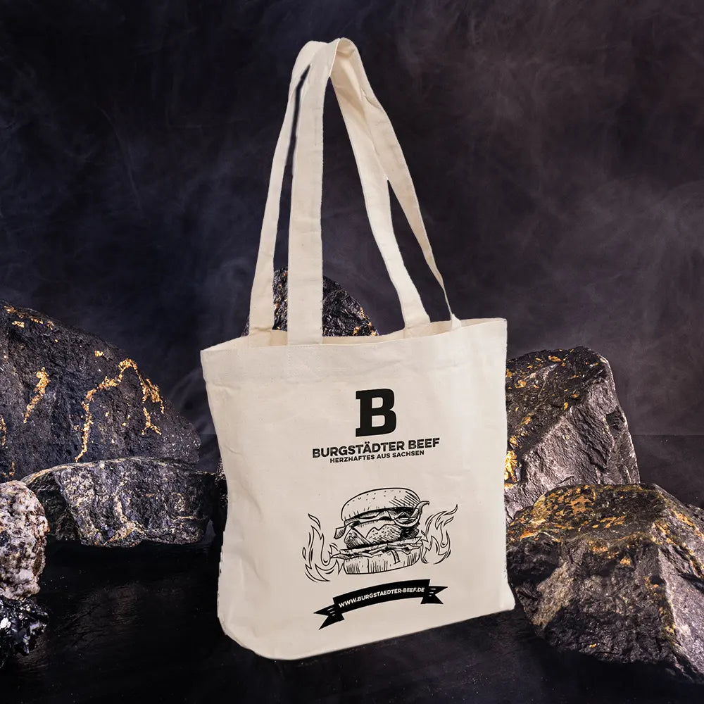 Weiße Stofftasche vor dunklem Hintergrund mit Felssteinen.