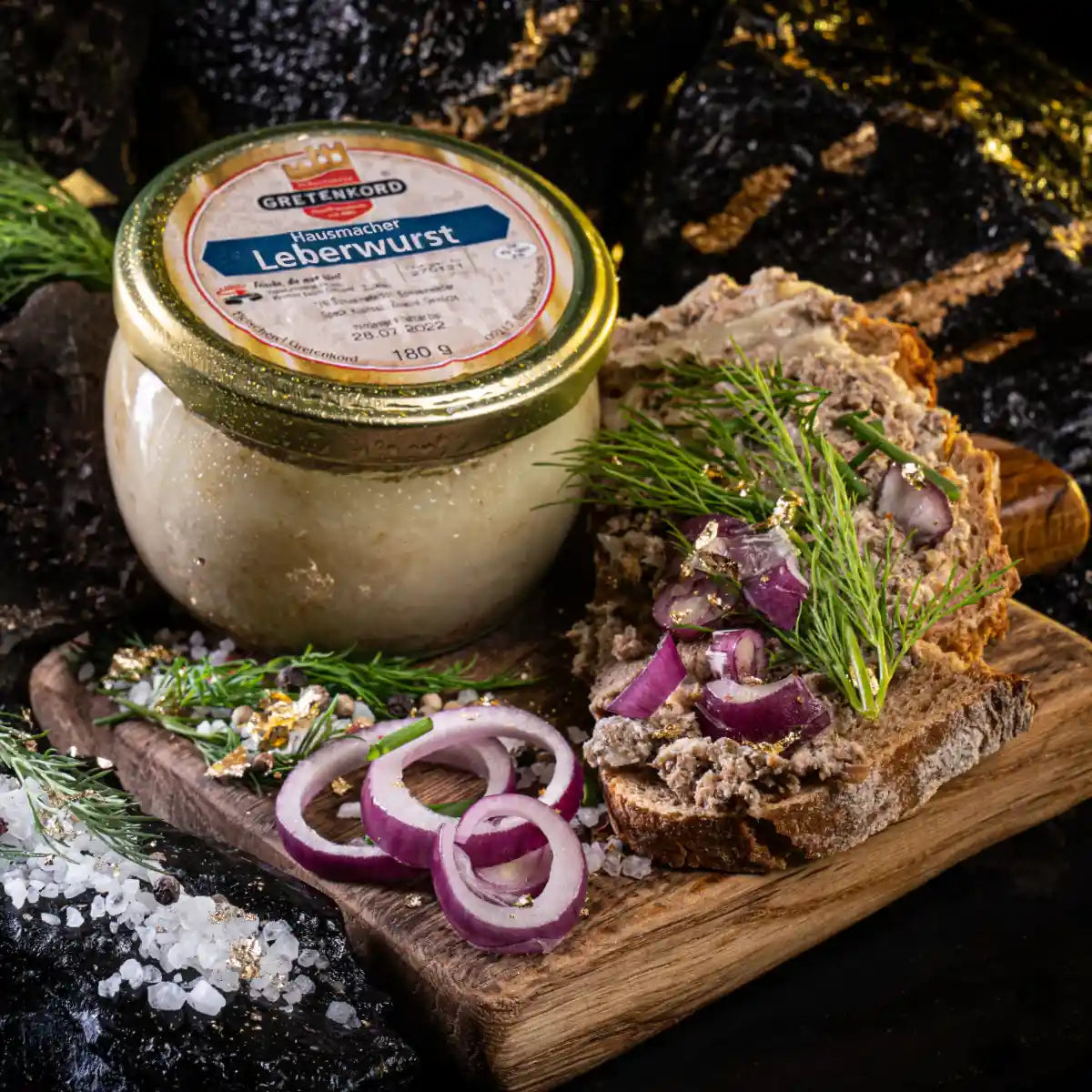 Ein geschlossenes Glas und daneben auf eine Scheibe Brot gestrichen Leberwurst mit roten Zwiebelringen dekoriert.