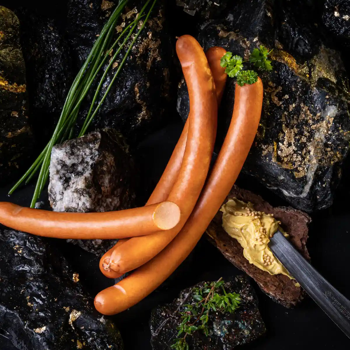 Mehrere große Wiener auf dunklem Untergrund mit einem Klecks Senf daneben