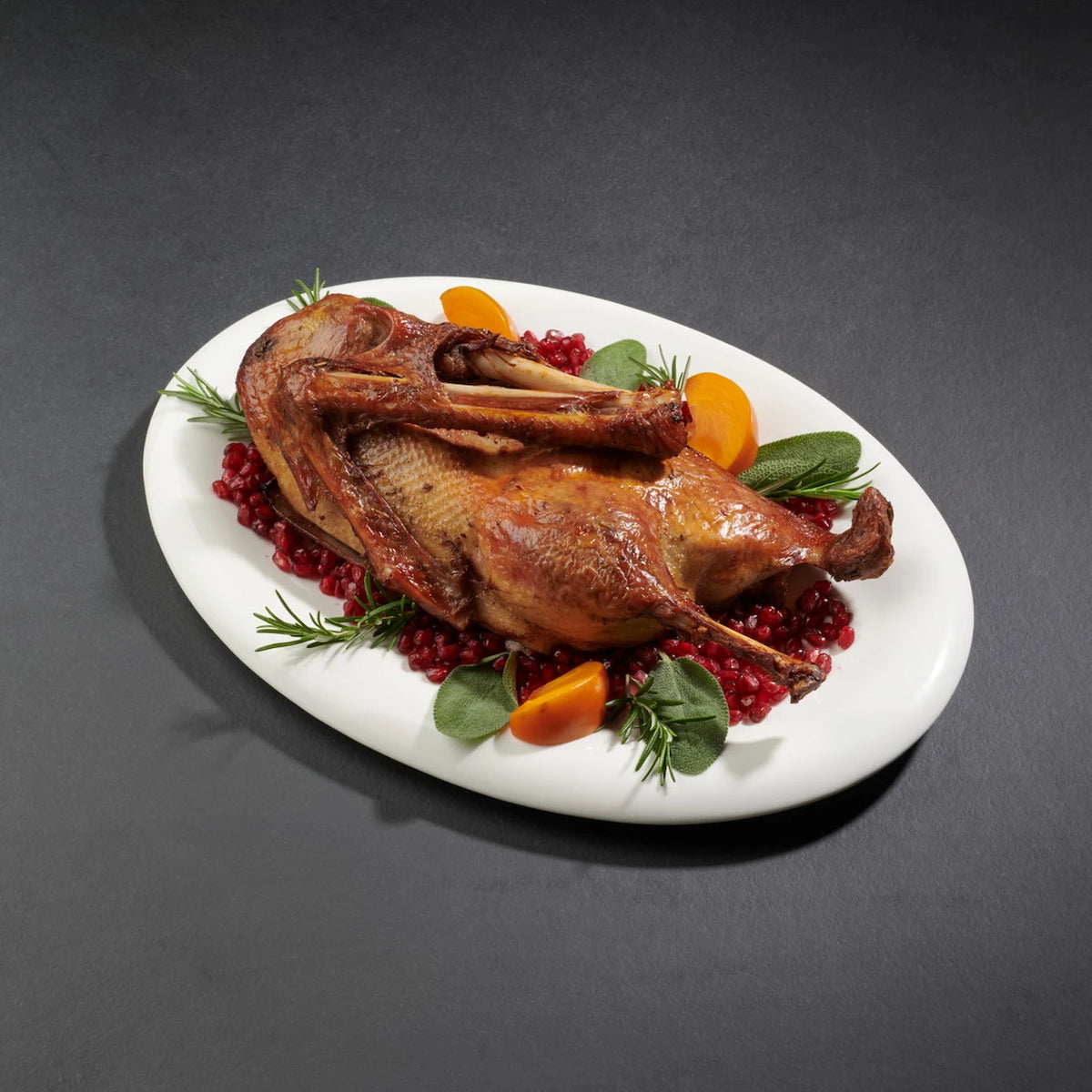Eine halbe Gans angerichtet auf einem weißen Teller mit Granatäpfeln, Gewürzen und Sharon Früchten.