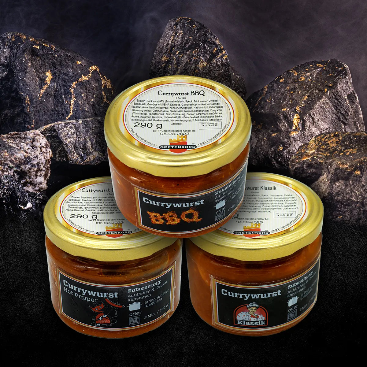 Drei verschlossene Gläser mit Currywurst vor auf schwarzem Untergrund vor Steinen