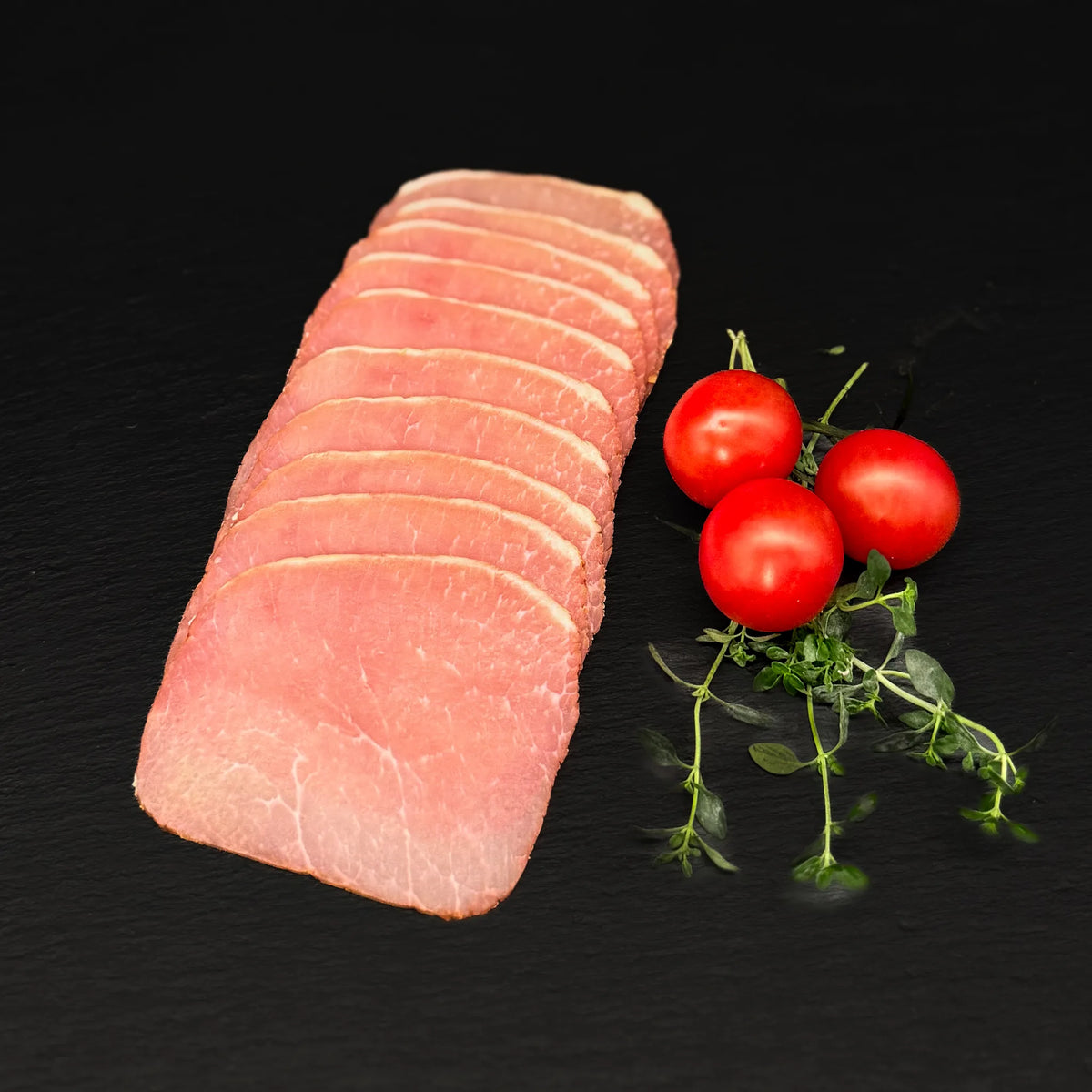 Geschnittener Lachsschinken, gefächert, auf einer schwarzen Schieferplatte mit Dekoration aus Tomaten und Kräutern.