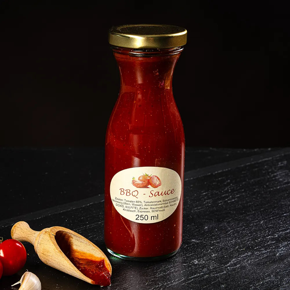 Rote BBQ Sauce in kleiner Glasflasche neben kleinem Holzlöffel vor dunklem Hintergrund.