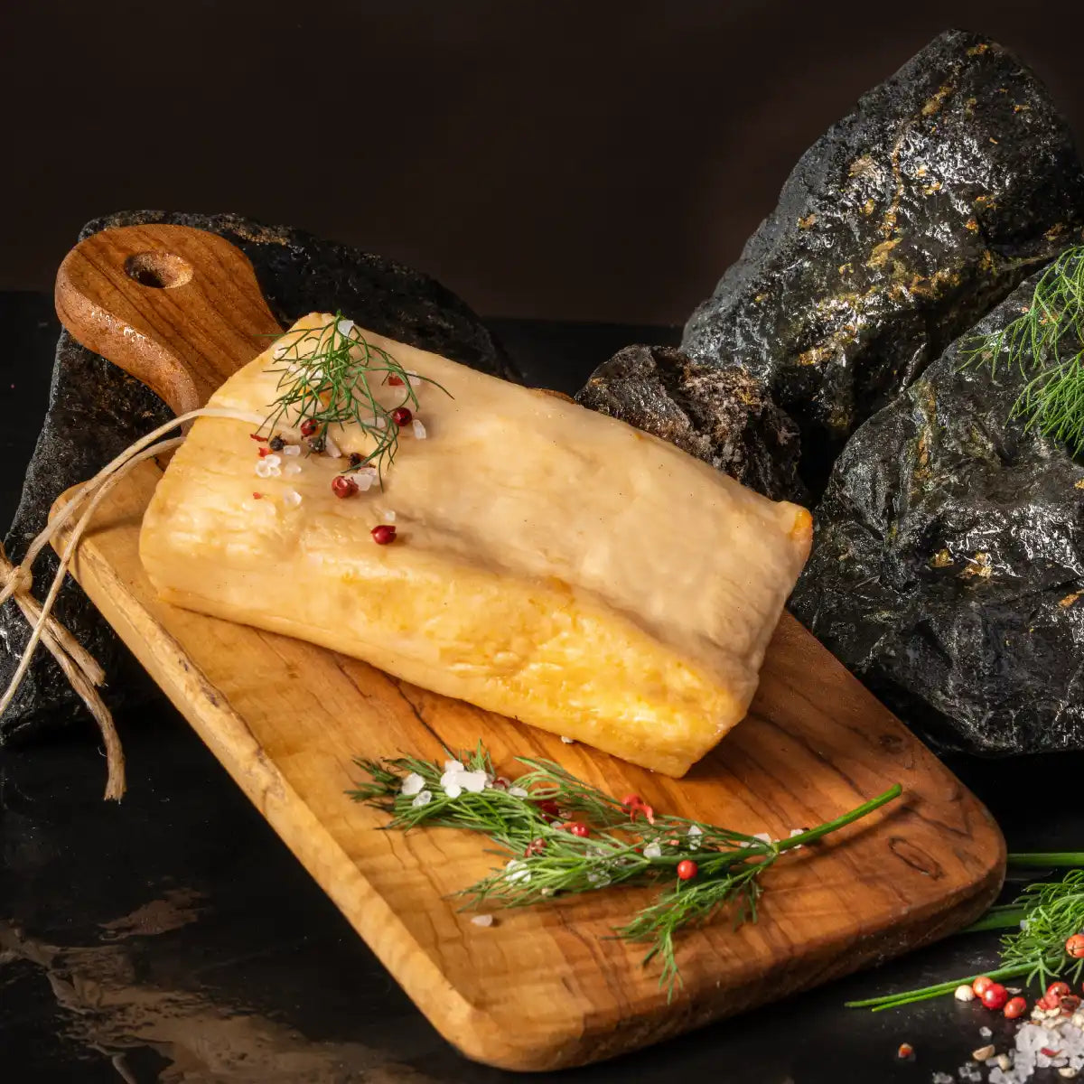 Ein ganzes Stück weißer Speck liegt auf einem hellen Holzbrett mit Salzkörnern garniert.