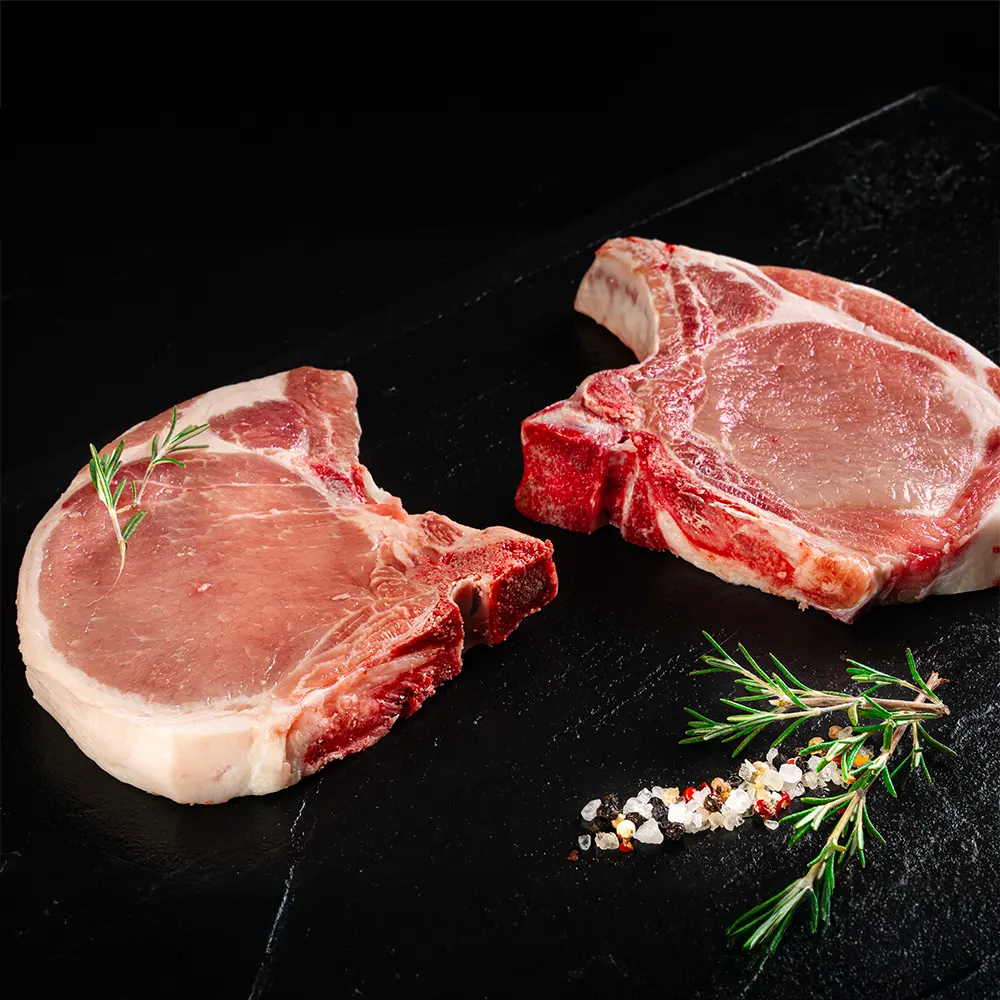 Zwei Kronenkotellets vom Duroc Strohschwein von der Seite vor dunklem Hintergrund.