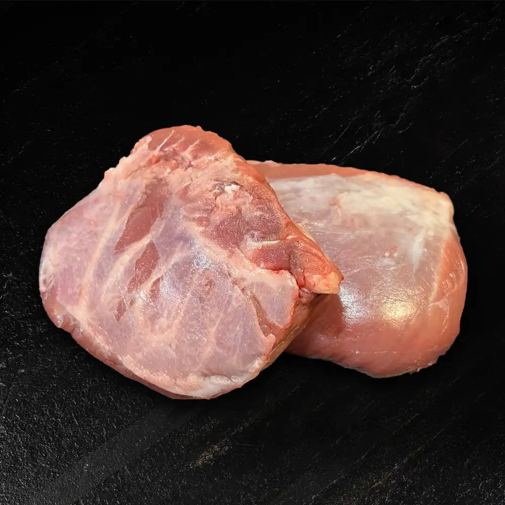 Zwei Schweinebäckchen liegen nebeneinander auf dunklem Hintergrund.