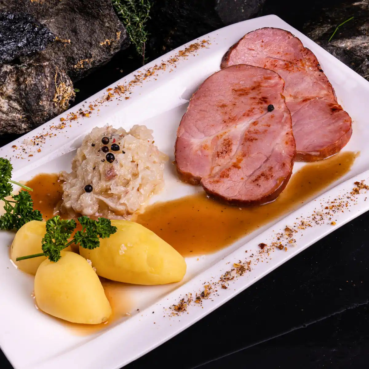 Gebratenes Kasseler auf einem weißen Teller angerichtet, mit Sauerkraut und Pellkartoffeln