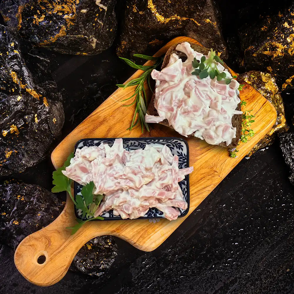 Fleischsalat auf zwei Brotscheiben auf einem Holzbrett. Dunkler Hintegrund mit Steinbrocken.