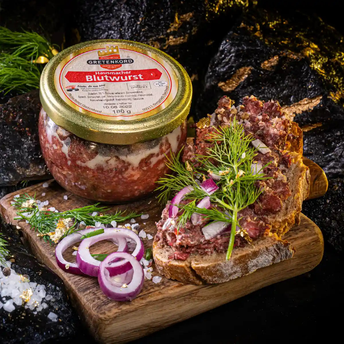 Ein Glas Hausmacher Blutwurst und daneben eine Scheibe Brot die damit bestrichen ist.