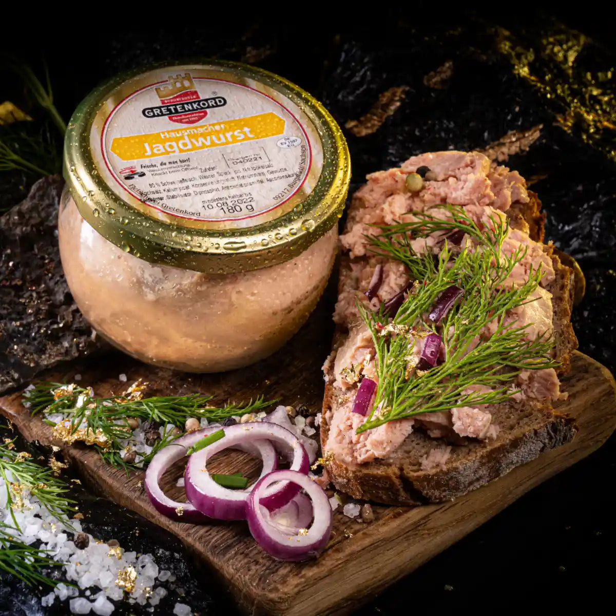 Ein Glas mit Hausmacher Jagdwurst und daneben ein Brot mit dem Aufstrich