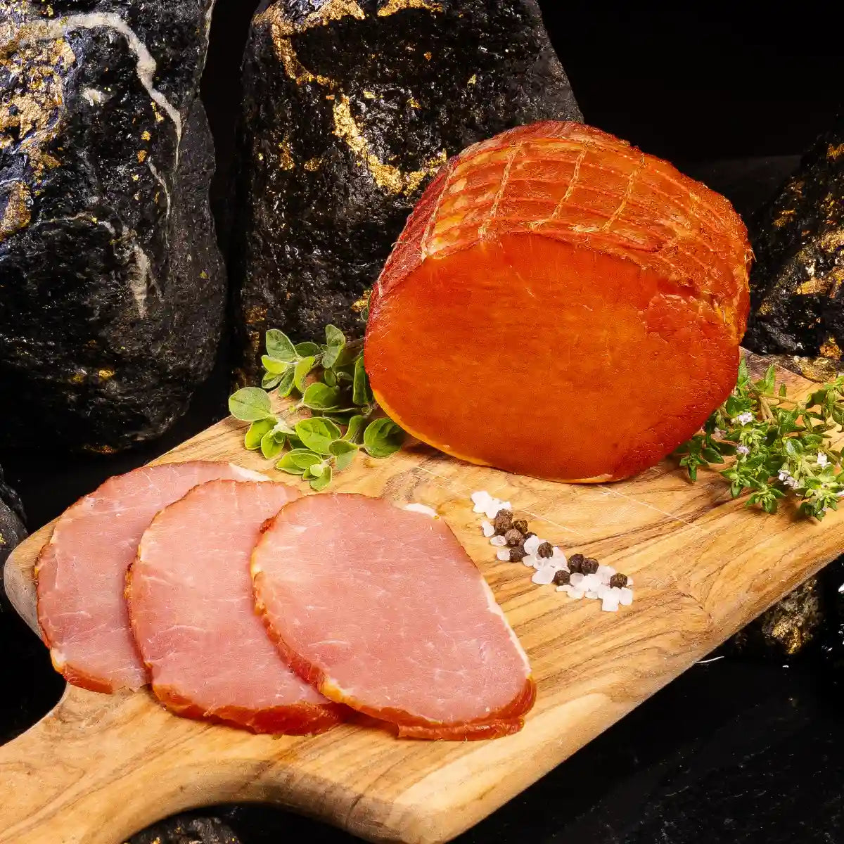Ein angeschnittenes großes Stück Lachsschinken und daneben einige Scheiben auf einem hellen Holzbrett