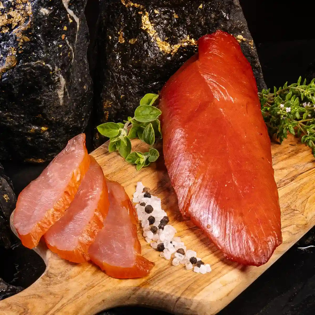 Ein Stück geräuchertes Putenfilet zusammen mit einigen aufgeschnittenen Stücken auf einem hellen Holzbrett