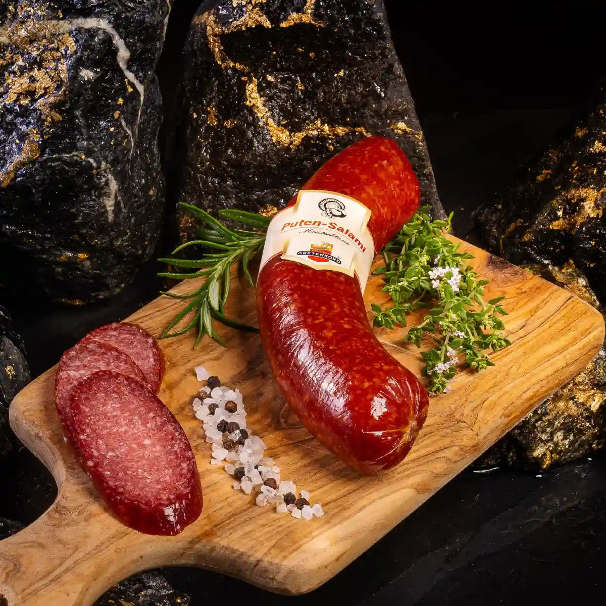 Ein Stück Putensalami im Darm auf hellem Holzbrett daneben aufgeschnittene Salamistücke