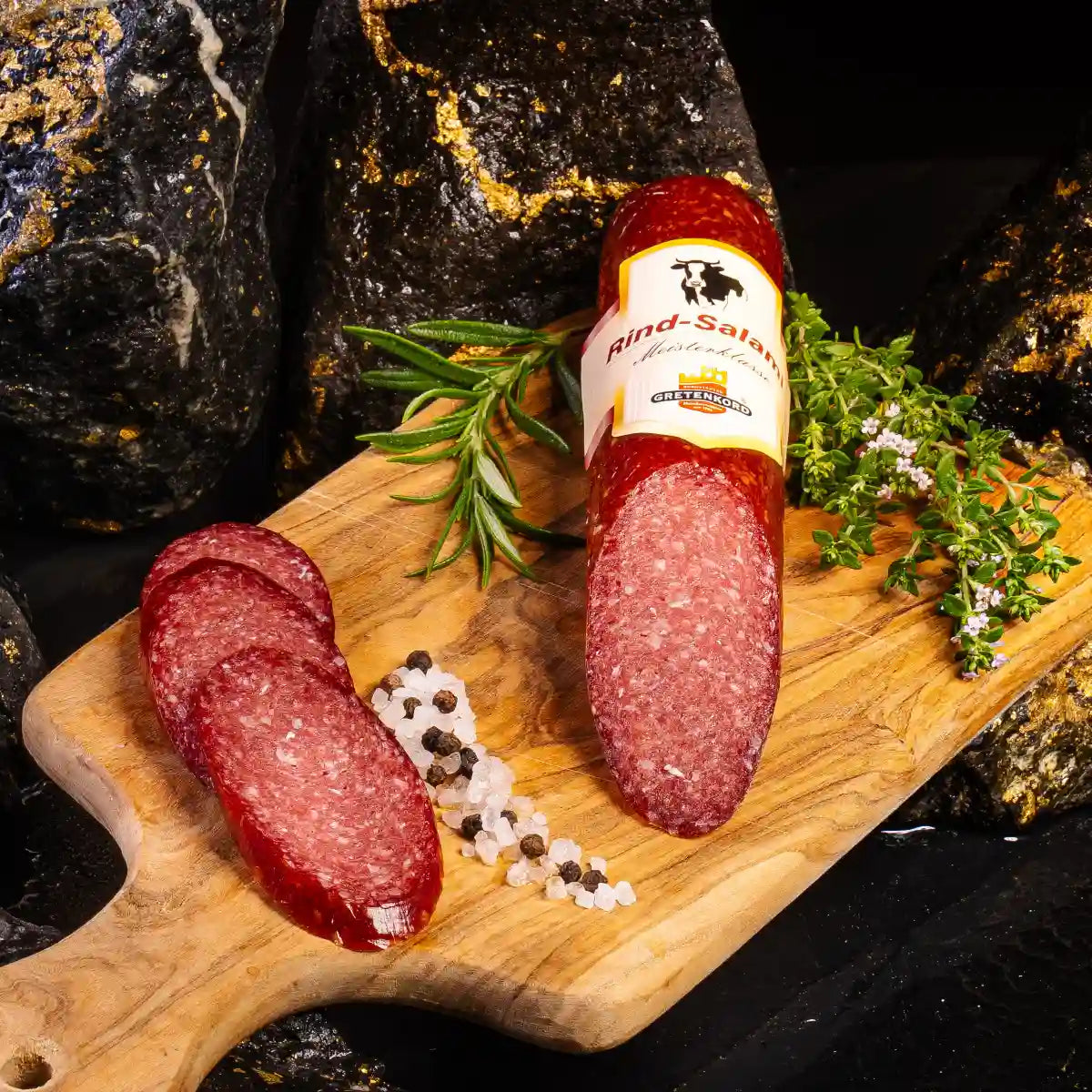 Ein angeschnittenes Stück Rindsalami auf hellem Holzbrett mit aufgeschnittenen kleinen Stücken daneben