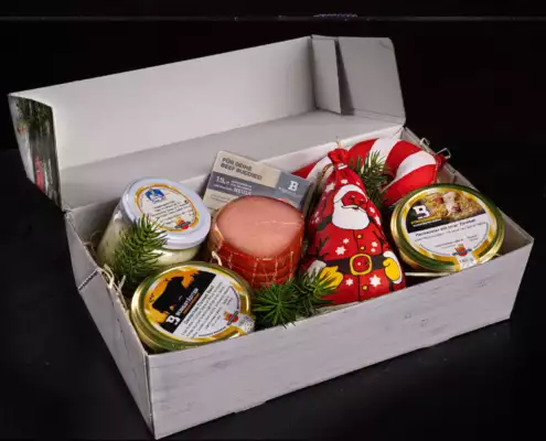 Eine Geschenkbox festlich gefüllt mit Weihnachtsmann- und Zuckerstangen-Salami, Lachsschinken und im Glas Corned Beef, Hubertusschmalz und Hackepeter