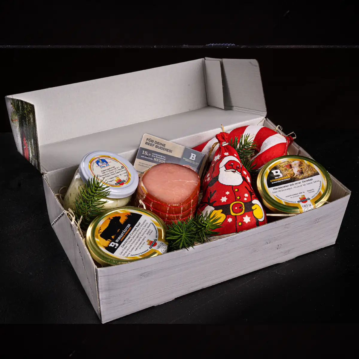 Eine Geschenkbox festlich gefüllt mit Weihnachtsmann- und Zuckerstangen-Salami, Lachsschinken und im Glas Corned Beef, Hubertusschmalz und Hackepeter