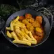 Eine gußeiserne Pfanne in der Pommes Frites und Currywurst mit gestreutem Curry angerichtet sind auf dunklem HIntergrund