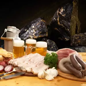 Gefüllte Biergläser und verschiedene Schlacht-Wurst-Delikatessen vor einem Stein-Hintergrund