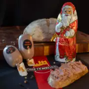 Zwei Leberwürste im Darm, daneben ein Schokoladen-Weihnachtsmann. Im Hintergrund ein Brotlaib im Vordergrund eine Brotscheibe mit Leberwurst bestrichen